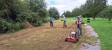 Group of people creating a meadow, one is operating machinery to scarify and prepare the ground for sowing.