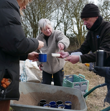 Volunteer serving hot drinks from a wheelbarrow
