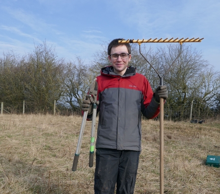 Volunteer James holding a rake and loppers