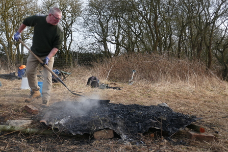 Volunteer beating down bonfire to manage the flames