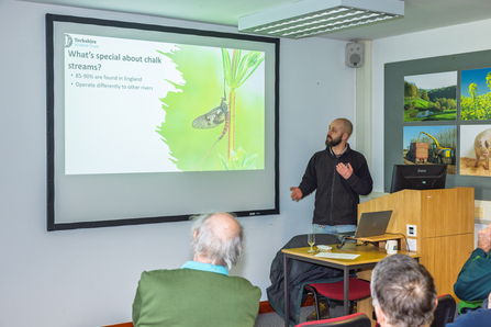 Calum standing before presentation asking 'what's so special about chalk streams?'