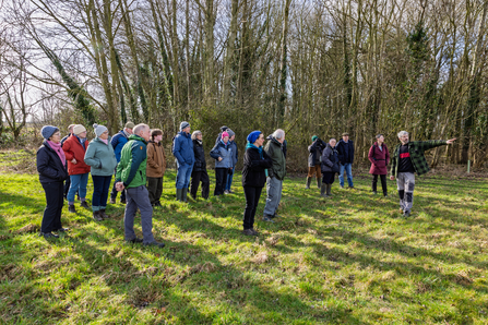 Group of volunteers in field listening to Jon explain the conservation works