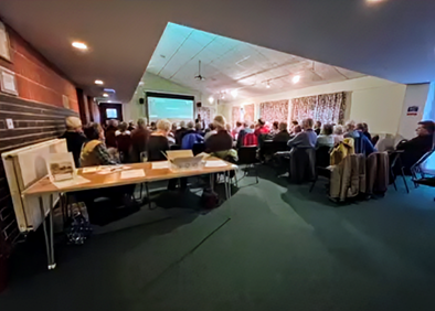 A meeting room with a large number of people.