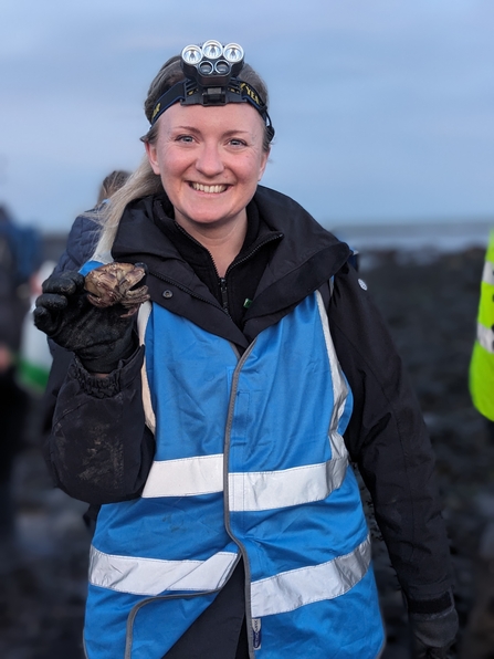 A smiling woman in a bright blue high-vis vest holds out a small grab