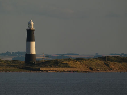 A coastal landscape with a lighthouse on the left and a calm sea in the foreground