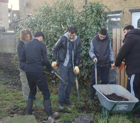 A group of four young men are digging out an area into a wheelbarrow