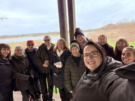 Group of birdwatching ladies gathered in front of a nature reserve looking at the camera