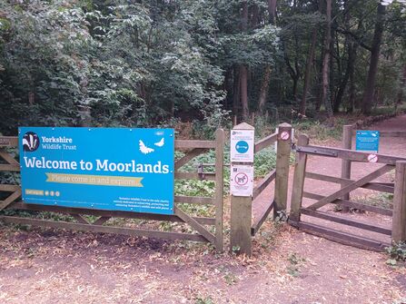 The image shows a large gate to the left with a blue sign on it, and a smaller pedestrian gate to the right.