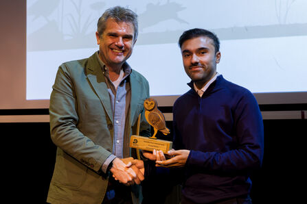 A young person stood on the right, Abdurrahan Butt, accepts an award from Wildlife Trusts CEO Craig Bennett (l)