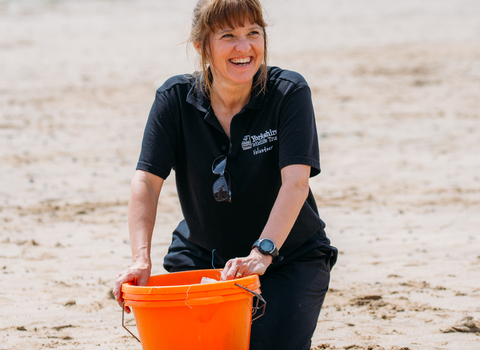 Emma Dawber, volunteer, smiling on beach with orange bucket