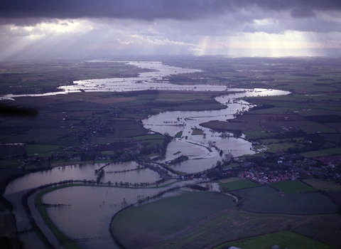 A drone image of the River Derwent meandering through the landscape with fields either side flooded. The sun is shining through the clouds.