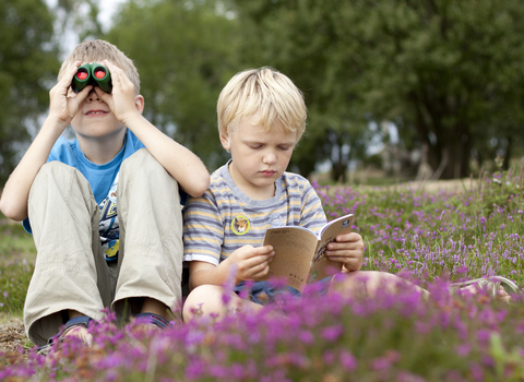 Two children sitting in heathland, one with binoculars and one with a Wildlife Watch book