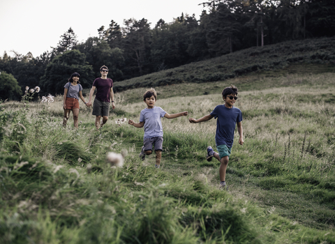 Two adults and two children running through a field
