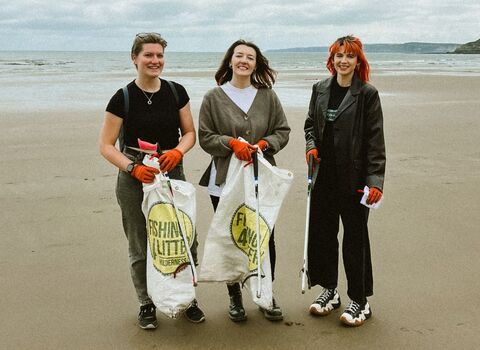 Three women stood facing the camera on a beach with litter picking bags