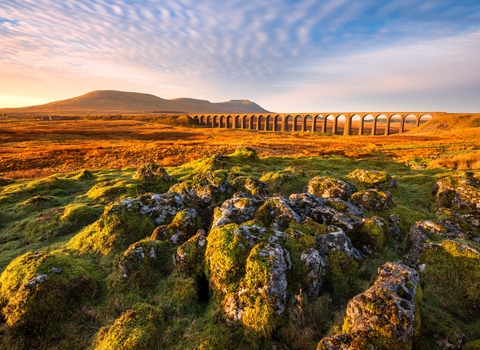 view of a viaduct railway bridge over the imestone pavement Yorkshire Dales with a mountain in the distance. 