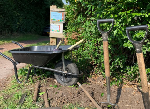 Kippax Wildlife Corridor - planting in action wheelbarrow in shot and their previous wildlife gardening awards depicted in the background
