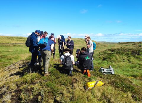A group of people on top of a small hill, looking at something in front of them with a blue sky above.