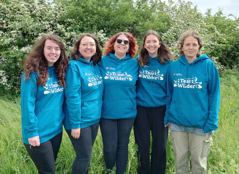 Five individuals wearing matching teal hoodies that say "I'm part of Team Wilder" stand in front of a white-flowered bush and green grass.