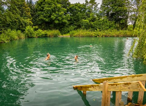 Two people swimming in a large outdoor, natural pool.