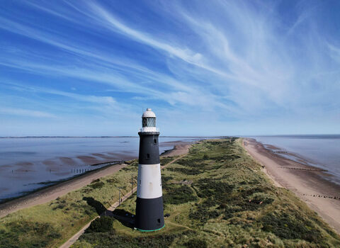 Lighthouse black and white striped in foreground. On a spit - grey sea either side with grassy land in the middle